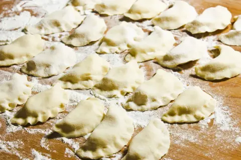 Surowe pierogi ułożone na drewnianej desce, posypane mąką.