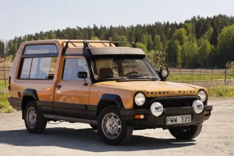 En orange Talbot Matra Rancho står parkerad på en grusväg med skog i bakgrunden.