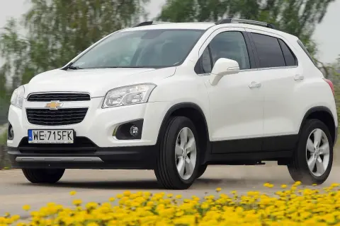 Biały Chevrolet Trax jedzie po drodze, otoczony żółtymi kwiatami.