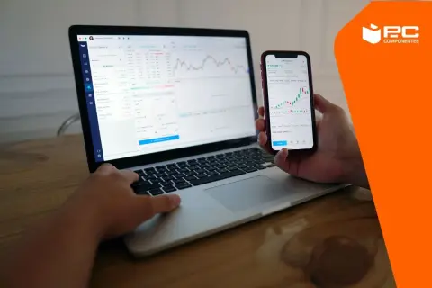 Persona usando un portátil y un móvil para conectar movil a pc y ver gráficos financieros.