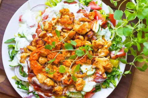 Talerz z kurczakiem kebab, warzywami, sosem i ziołami.