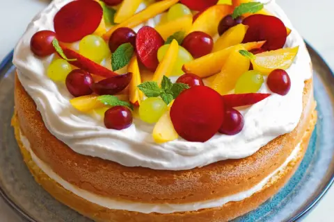 Torta compleanno pan di spagna con panna montata e frutta fresca: pesche, uva rossa e bianca, prugne e foglioline di menta.