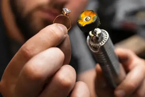 Manos de joyero puliendo un anillo de oro con un diamante. La herramienta de pulido tiene una placa de oro en su extremo.