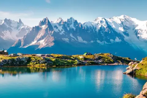 Lac alpin paisible reflétant les sommets enneigés du Mont-Blanc. Un campement discret et un randonneur contemplent ce paysage grandiose, parfait pour une randonnée tour du mont blanc.