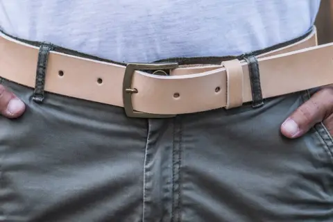 Uomo con cintura in cuoio chiaro, fibbia in ottone. La cintura si mette da che parte si desidera, ma solitamente a sinistra per comodità.