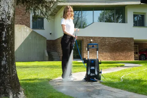 Donna usa idropulitrice per pulire il sentiero di cemento, mostrando come togliere il muschio.