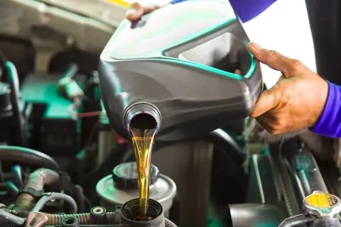 Händer häller ny motorolja i en bilmotor. Det är dags att byta olja, annars blir motorolja gammal och skadlig för motorn.