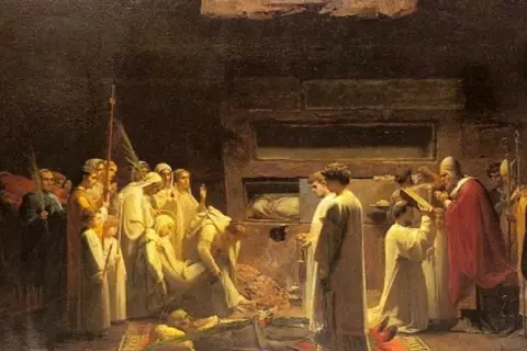 Scena religijna, gdzie wierni modlą się przy grobie. Czy można prosić zmarłego o pomoc? Obraz ukazuje ludzi w białych szatach, duchownych i trumny.