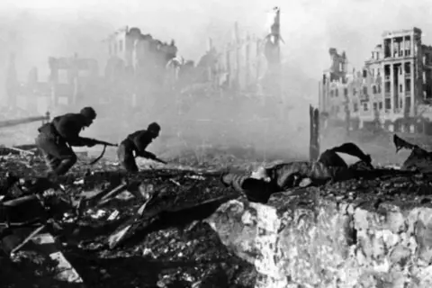 Soldater kämpar i ruiner. En fallen soldat ligger framför dem. Detta är en bild från slaget om Stalingrad, som idag heter Volgograd.