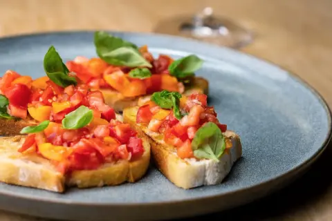 Bruschetta mit Tomaten und Basilikum auf einem grauen Teller.
