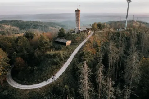 Radfahrer auf einem Weg zum Aussichtsturm Bergneustadt. Der Turm thront über einer bewaldeten Hügellandschaft.