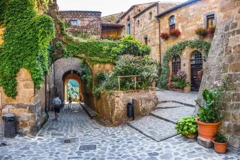Un vicolo acciottolato tra antichi edifici ricoperti di edera e fiori, un invito a scoprire i borghi da visitare nelle Marche.