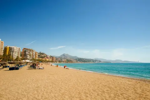 Playa con sombrillas y tumbonas, gente disfrutando del sol y el mar. ¡Unas de las mejores playas cerca de Madrid!