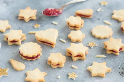 Sterne und Herzen aus veganen Keksen mit Marmeladenfüllung, dekoriert mit glitzernden Sternen.