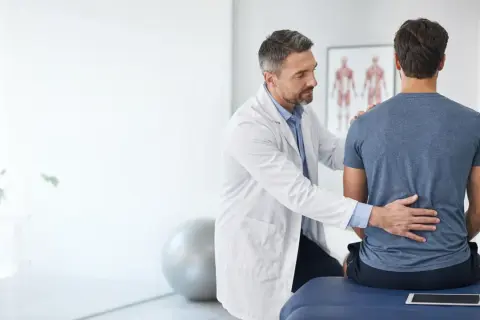 Medico esamina la schiena di un paziente, illustrando la differenza tra fisiatra e ortopedico.