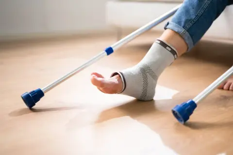 Osoba w ortezie na stawie skokowym próbuje chodzić z kulami. Rehabilitacja po artrodezie stawu skokowego wymaga cierpliwości.