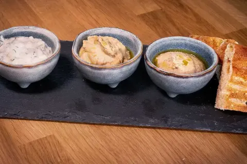 Tre skålar med dipp, en med dill, och två med en smak av 7 kryddor, serveras med rostat bröd på en stenplatta.