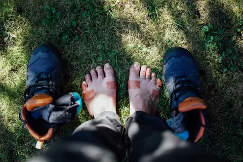 Fötter med plåster och vandringsskor på gräs. Kanske dags för nya vandringsstrumpor sommar?