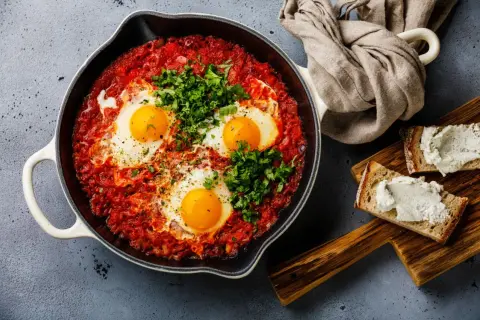 Herzhafte Eier in Tomatensoße, garniert mit Petersilie. Perfekt für schnelle Gerichte, serviert mit Brot und Frischkäse.