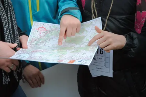 Dłonie wskazują trasę na mapie podczas biegu na orientację.