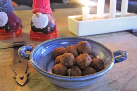 En blå skål med chokladpraliner, perfekta som julgodis utan socker. I bakgrunden syns tomteljus och adventsljusstake.