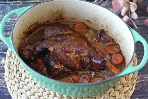 Un gigot de 7 heures mijoté dans une cocotte verte, avec des carottes et des oignons. La viande est tendre et dorée, prête à être dégustée.