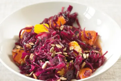 Rotkohlsalat mit Apfel und Orange, garniert mit Sonnenblumenkernen, in einer weißen Schüssel.