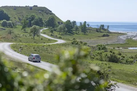 En bil kör på en slingrande väg längs Gotlands kust. Perfekta gotlandstips för en bilsemester.