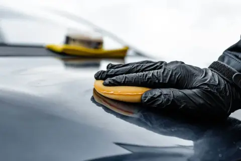 Rękawiczka w czarnej rękawicy rozprowadza wosk na ceramice, nadając jej połysk.
