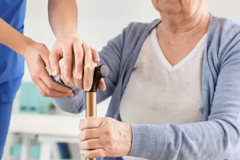Opiekunka wspiera starszą panią z laską, symbolizując troskę i nowoczesne metody leczenia parkinsona.