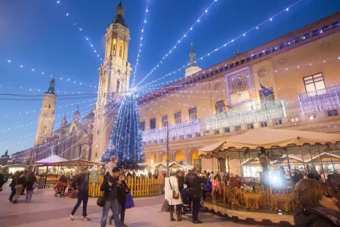 Mercado navideño en Zaragoza con árbol iluminado y gente paseando. Descubre qué ver en Zaragoza en Navidad.