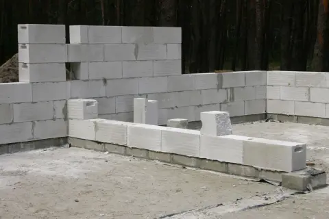 Budowa domu z betonu komórkowego. Ściany wznoszone z białych bloczków, w tle las.