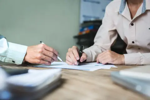 Dwie osoby przy biurku analizują dokumenty. Jedna z nich pisze, druga wskazuje coś na papierze. Może to być pomoc w procesie jak odzyskać pieniądze z obligacji Getin Noble Bank.