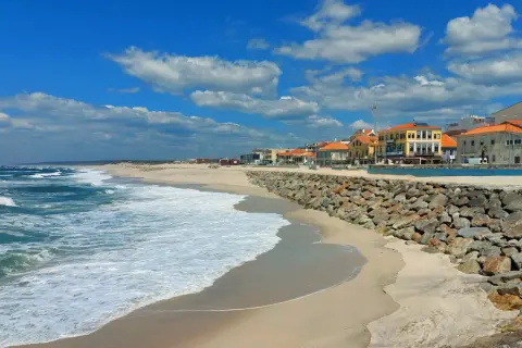 Sonne, Sand und Wellen an der Costa Verde, Portugal. Häuser mit roten Dächern säumen den Strand, geschützt von einer Steinmauer.