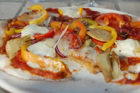 En pizza med surdegsbotten, toppad med mozzarella, paprika, tomat, rödlök och kronärtskocka.