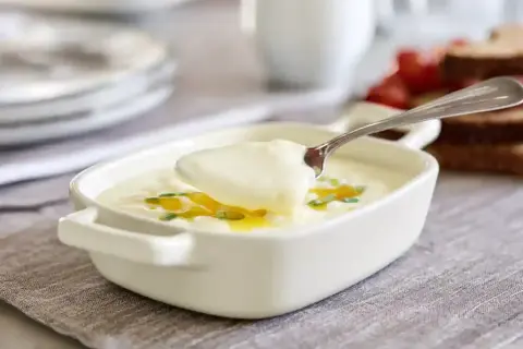 En sked lyfter krämig bechamelsås ur en vit skål, perfekt för ditt bechamelsås recept.