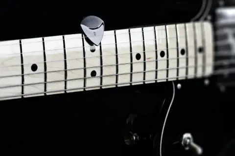 Nahaufnahme eines Plektrums auf den Saiten einer Gitarre. Perfekt, um die **Gitarre Saitenlage einstellen** zu lernen.