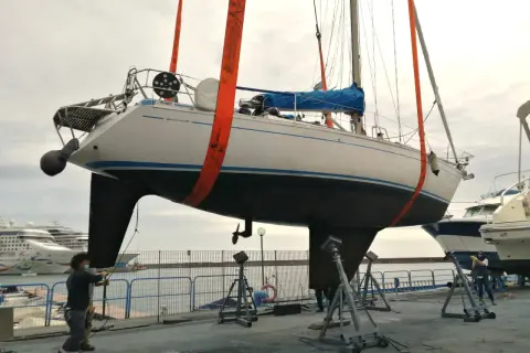Barca a vela sollevata da gru, pronta per la manutenzione dello scafo e l'applicazione dell'antivegetativo.