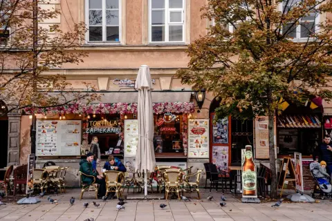Jesienna Polska na weekend: kawiarnia z zapiekankami i grzanym winem, ludzie siedzą przy stolikach, gołębie spacerują po bruku.