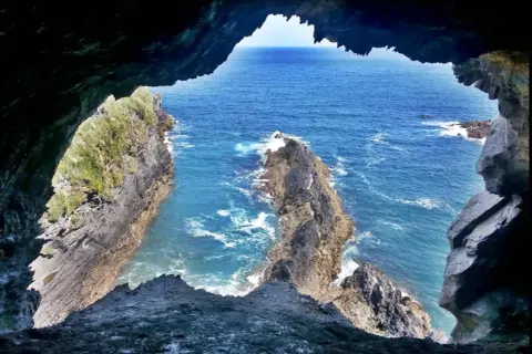 Vista desde la Cova da Doncela hacia el mar azul y acantilados rocosos.