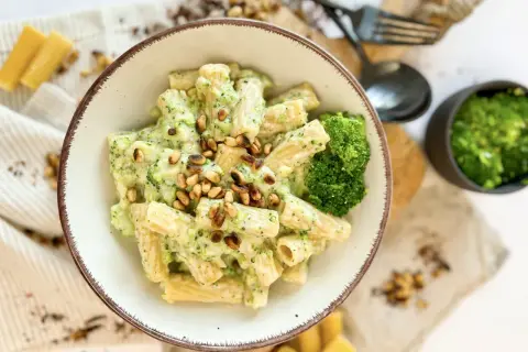 Eine Schüssel Rigatoni mit cremiger **Brokkoli Sahne Sauce** und Pinienkernen garniert. Daneben ein kleiner Napf mit gehacktem Brokkoli und Käse.