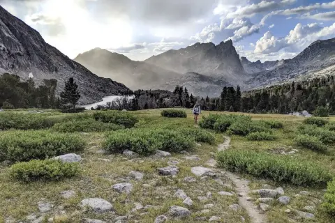 Wanderer auf dem Continental Divide Trail wandern durch eine bergige Landschaft mit einem See und bewaldeten Hängen.