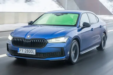 Niebieska Skoda Superb 2.0 TSI pędzi po mokrej drodze, tworząc wrażenie prędkości.