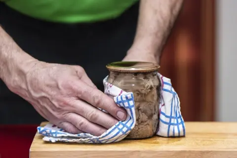 Mężczyzna używa ściereczki, by łatwiej otworzyć słoik z mięsem.