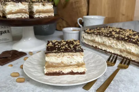 Pyszne ciasto bez pieczenia maxi king z warstwami kremu, karmelu i czekolady, posypane orzeszkami.