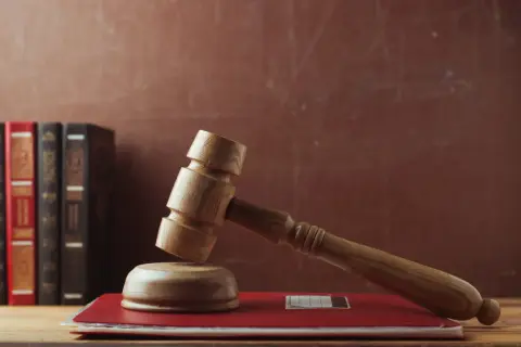 Martelletto da giudice su un libro rosso, con libri legali sullo sfondo. Rappresenta il **significato** di interdizione e giustizia.