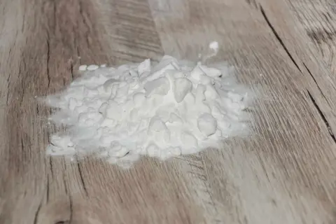 Ein Haufen weißes Pulver, wahrscheinlich Natriumascorbylphosphat, liegt auf einer Holzoberfläche.