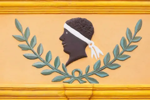 Bas-relief d'une tête d'homme noir, ornée d'un bandeau blanc, entourée de feuilles de laurier. Une évocation des maures origine.