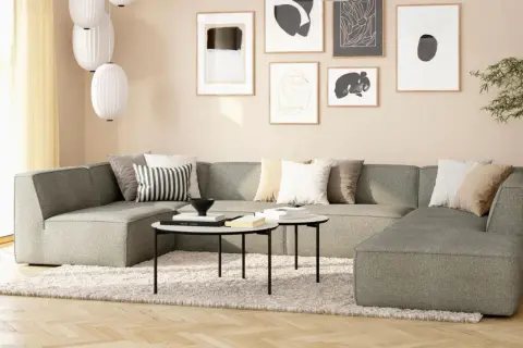 Gemütliches Wohnzimmer mit beiger Wand, einem großen grauen Sofa, Kissen und Kunstwerken.