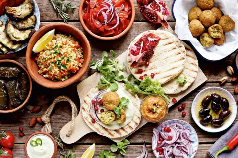 Vielfalt an arabischem Essen: Falafel, gefüllte Weinblätter, Bulgursalat, gegrilltes Gemüse, Hummus, Oliven und Granatapfel.